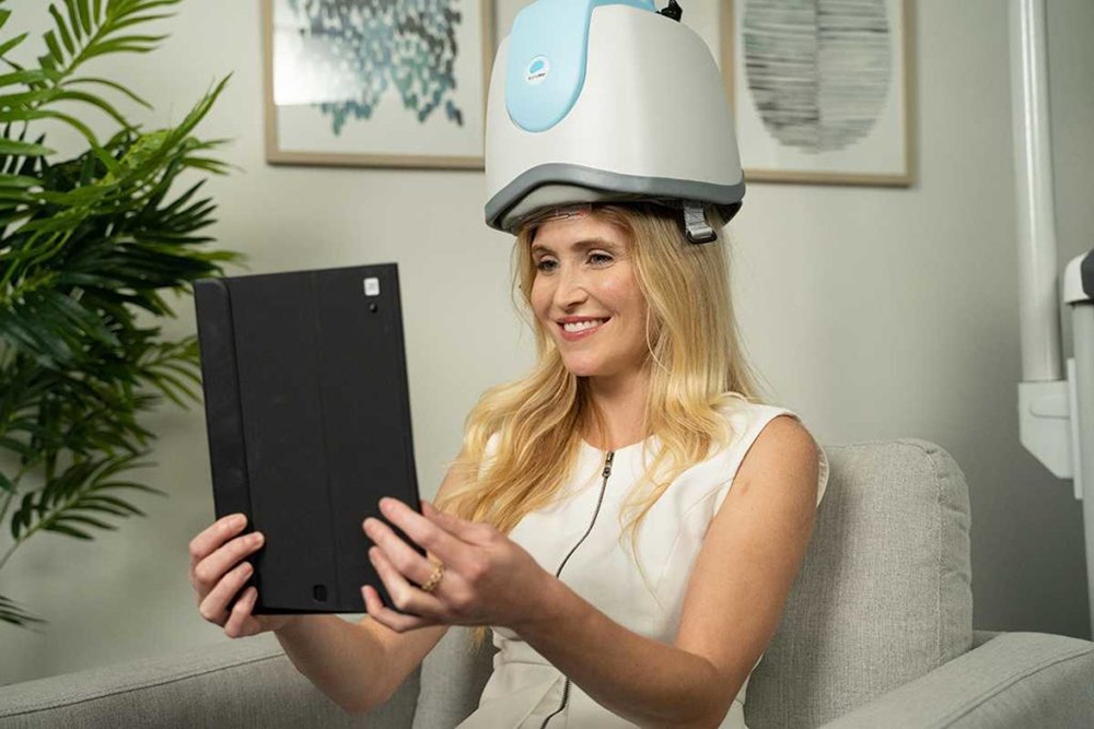 A smiling lady relaxing with her tablet while using a TMS machine.
