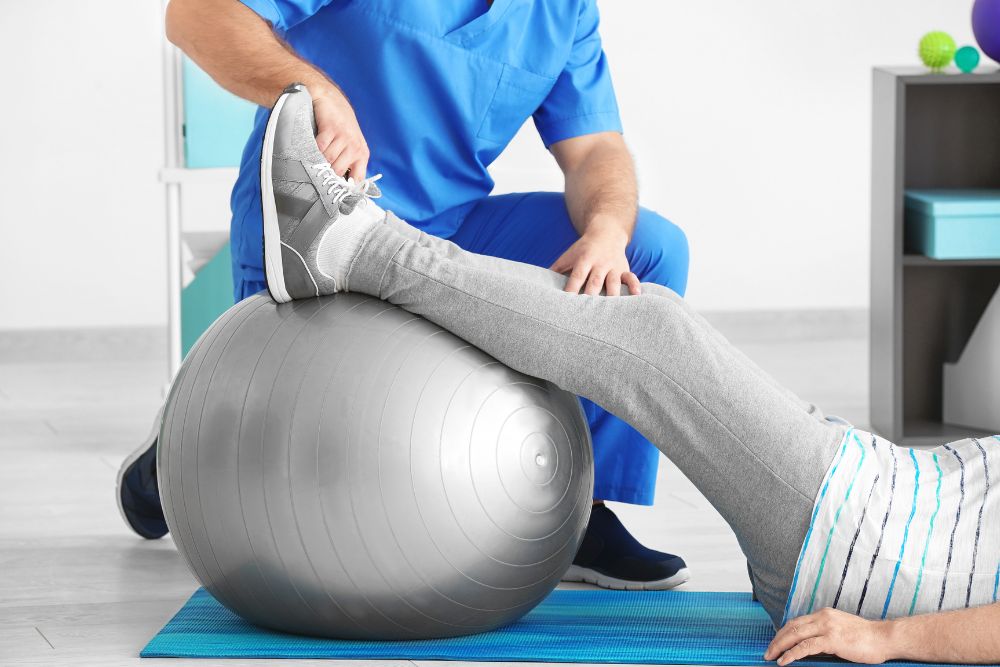 A patient doing leg raise exercises on a grey balance ball for East Norriton vestibular disorder treatment.