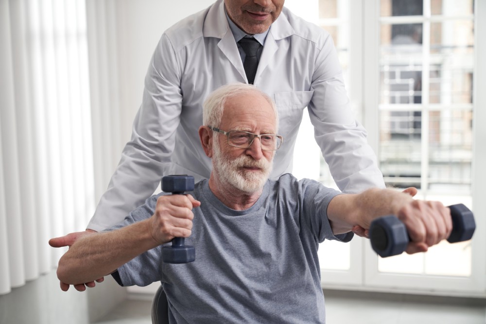 An elderly man doing arm exercises with small weights as part of Parkinson's treatment near King of Prussia, Pennsylvania.