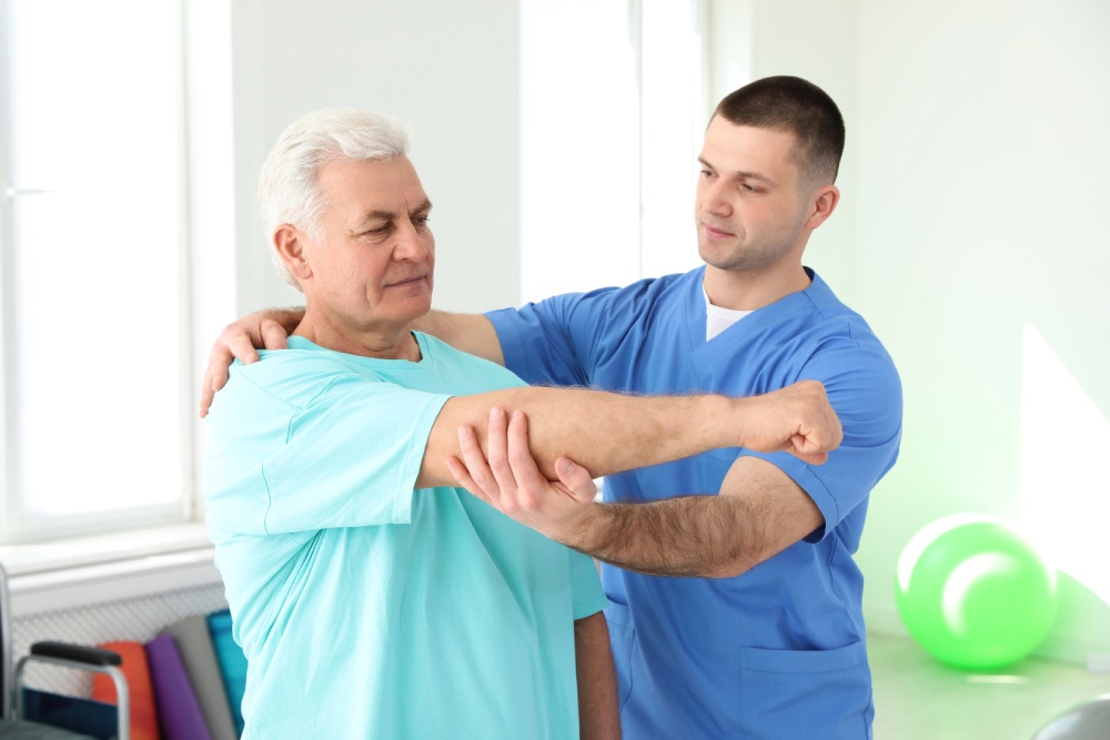 A male patient doing an arm exercise guided by a Trooper stroke rehab physical therapist.